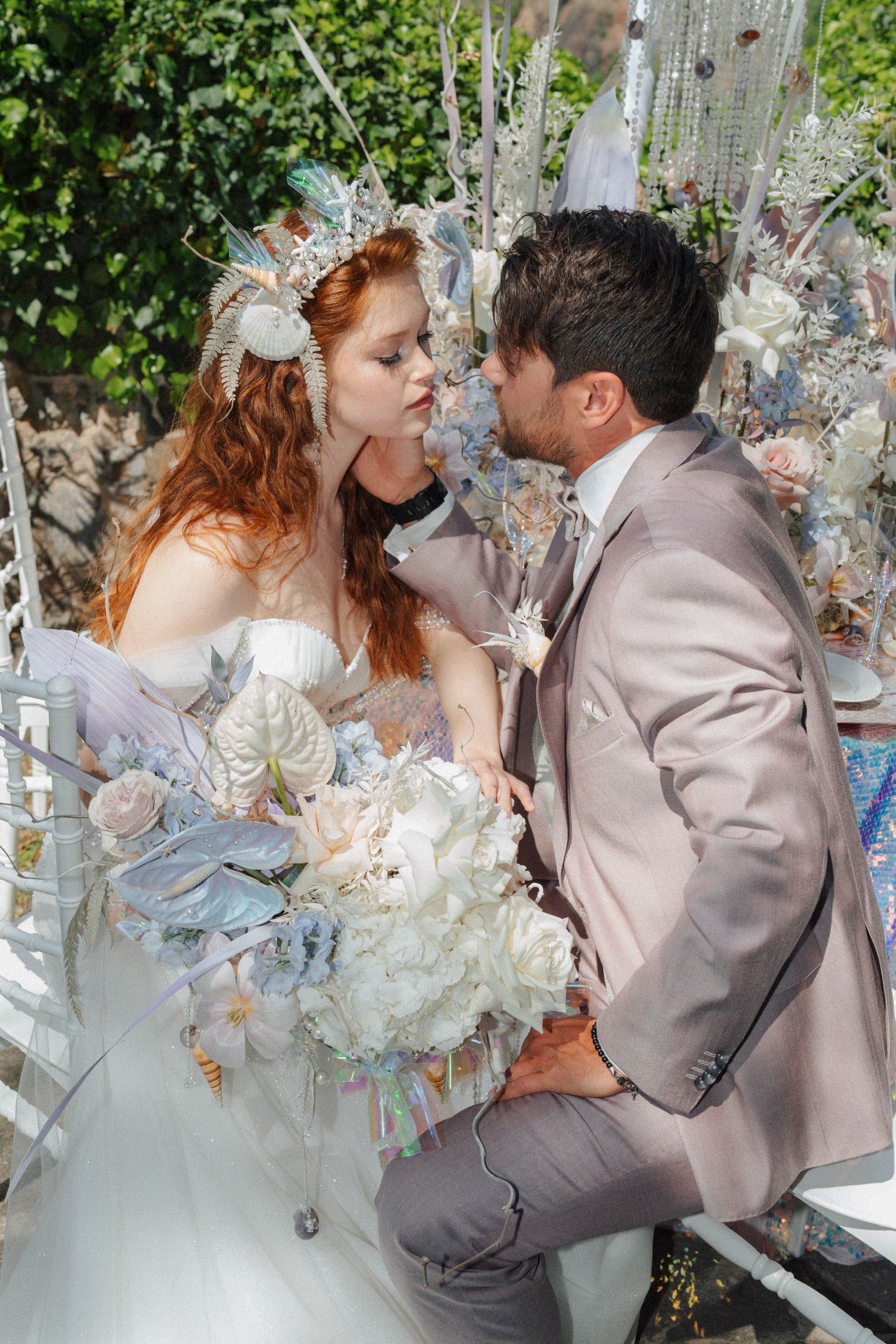 Brautpaar am Hochzeitstisch mit verspielter Bilderbuch-Floristik im Ariell die Wassernixe-Motto mit Anthurien, Rosen, Nelken. Bruat mit Kopfschmus Flowerkron mit Muscheln, Perlen und Federn