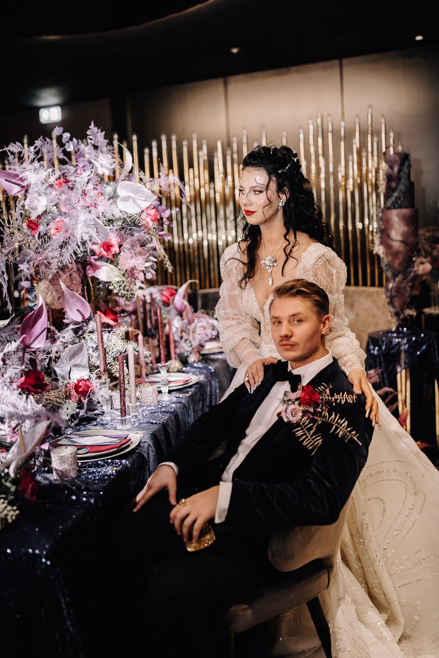 Influencer-Brautpaar am Hochzeitstisch mit Dekoration von Zanoza. Dekoration aus lila Anthurien, roten Rosen, Stabkerzen, Servietten und blauer Tischdeke