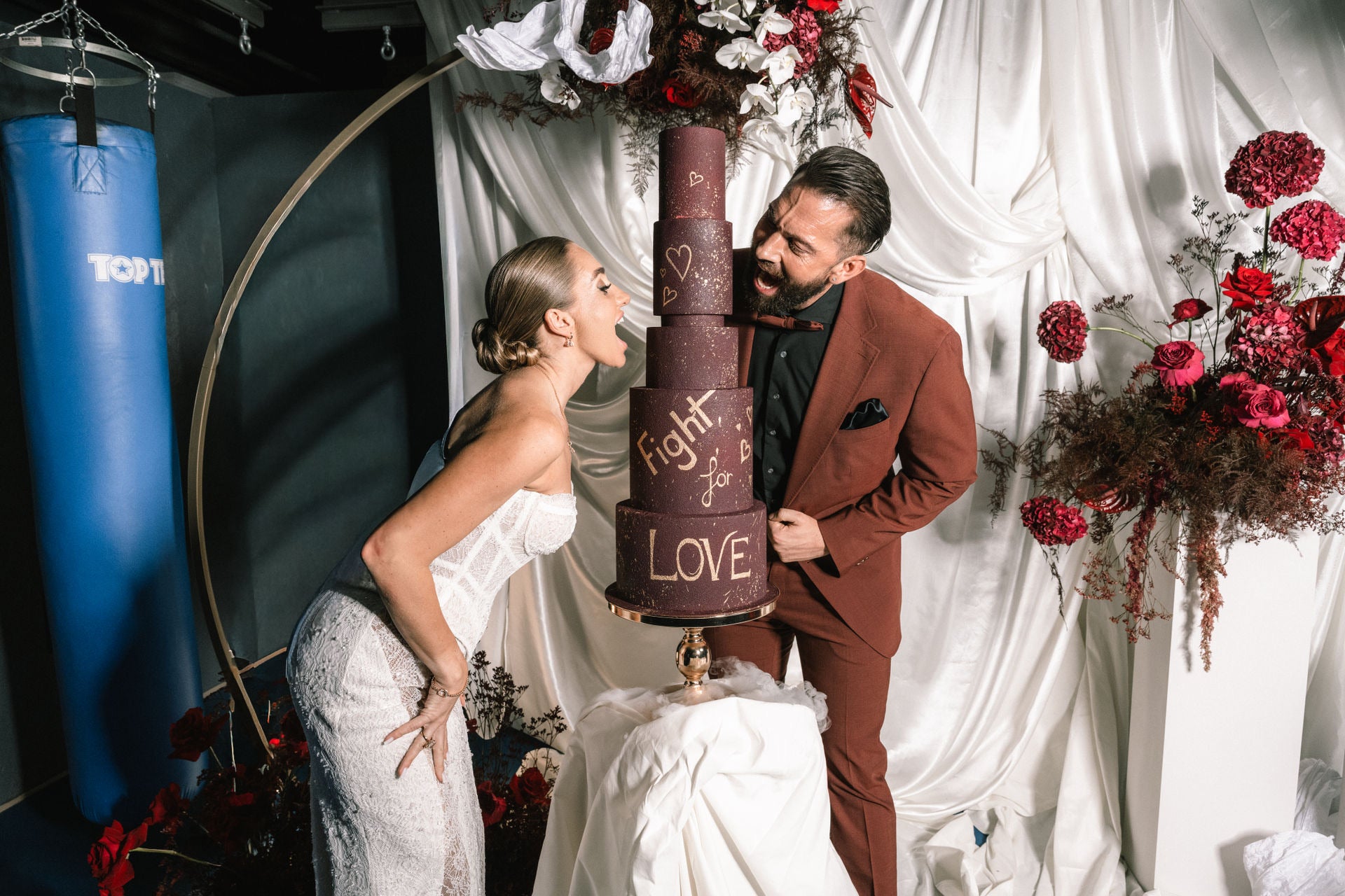 Brautpaar mit XXL-Torte in weinrot mit Aufschrift Fight for Love als Anspielung auf Hobby Boxen