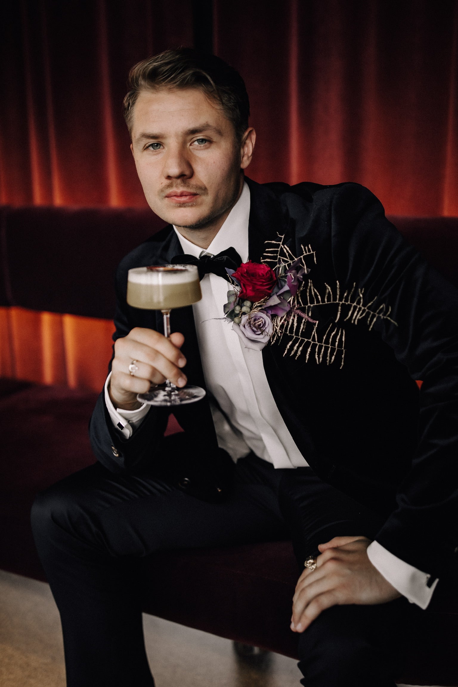 Influencer Richard Cwiertnia mit Signature Drink Cocktail mit Anstecker für Bräutigam mit roten und lila Rsen